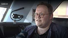 Screenshot aus einem Beitrag des SWR, auf dem ein Lokführer in einer Lok interviewt wird.
