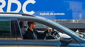 Ein Mann fährt mit einem Auto an einer blauen Lok mit RDC-Schriftzug vorbei.