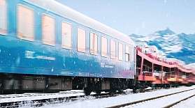 Der BTE AutoReiseZug fährt durch Schneelandschaft vor Bergkulisse.