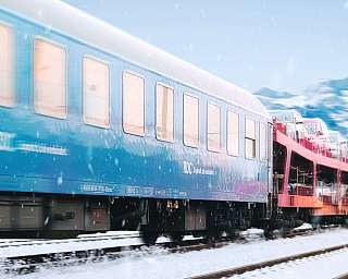 Der BTE AutoReiseZug fährt durch Schneelandschaft vor Bergkulisse.